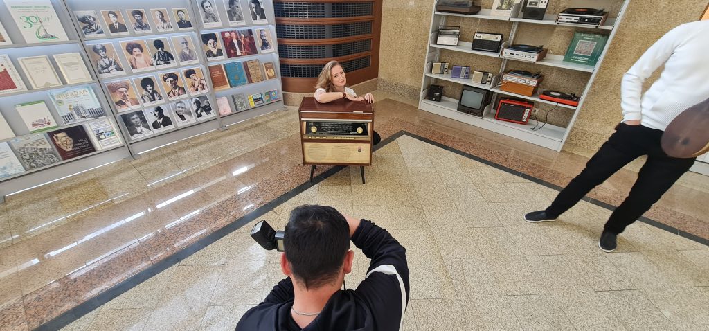 Kate Bass in front of an old Soviet style radio as photographer takes her picture in the foreground