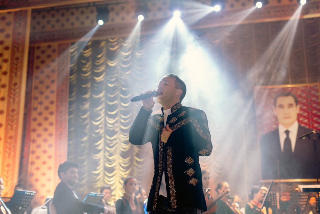 Richie "Robot" Steighner singing into a microphone with a spotlight on him in Turkmenistan