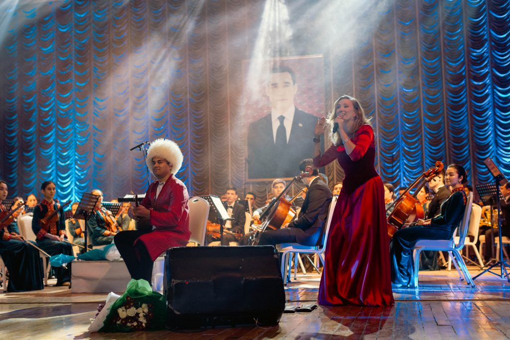 Sohbet Annamyradov and Kate Bass performing on stage with dutar and the Turkmenistan orchestra