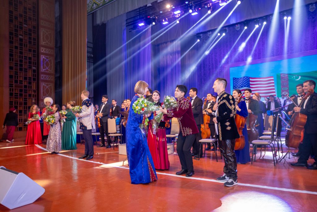 Ambassador Elizabeth Rood handing flowers to Dovran Shammyyev on stage in Turkmenistan